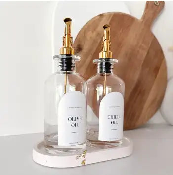 Clear glass olive oil and chili oil dispensers with gold-tone pump tops.